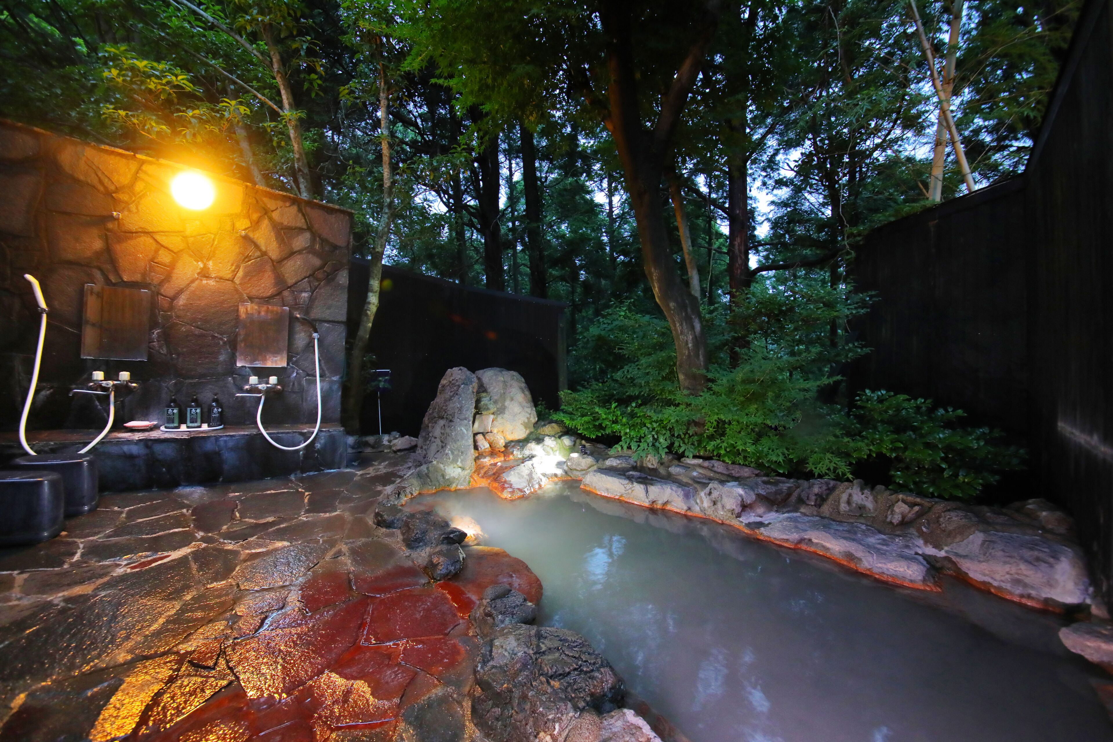 A stone hot spring area with a stone wall and wooden benches.