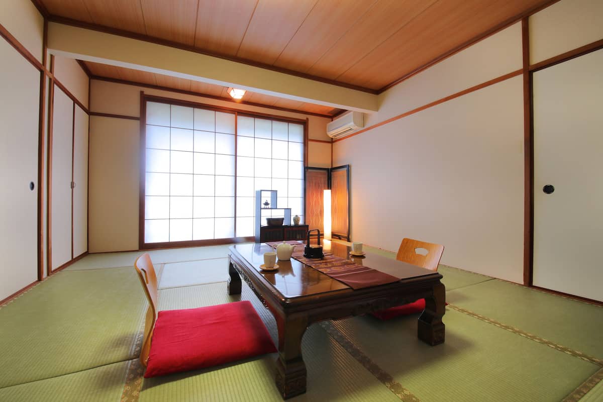 Um quarto tradicional japonês com piso de tatame, uma mesa de madeira baixa e portas deslizantes.