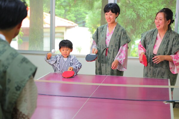 A room with a ping pong table, a window with a view of trees, and a person playing.