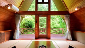 Un interior de madera con un ventanal grande, un esterilla de tatami y un juego de té japonés tradicional.
