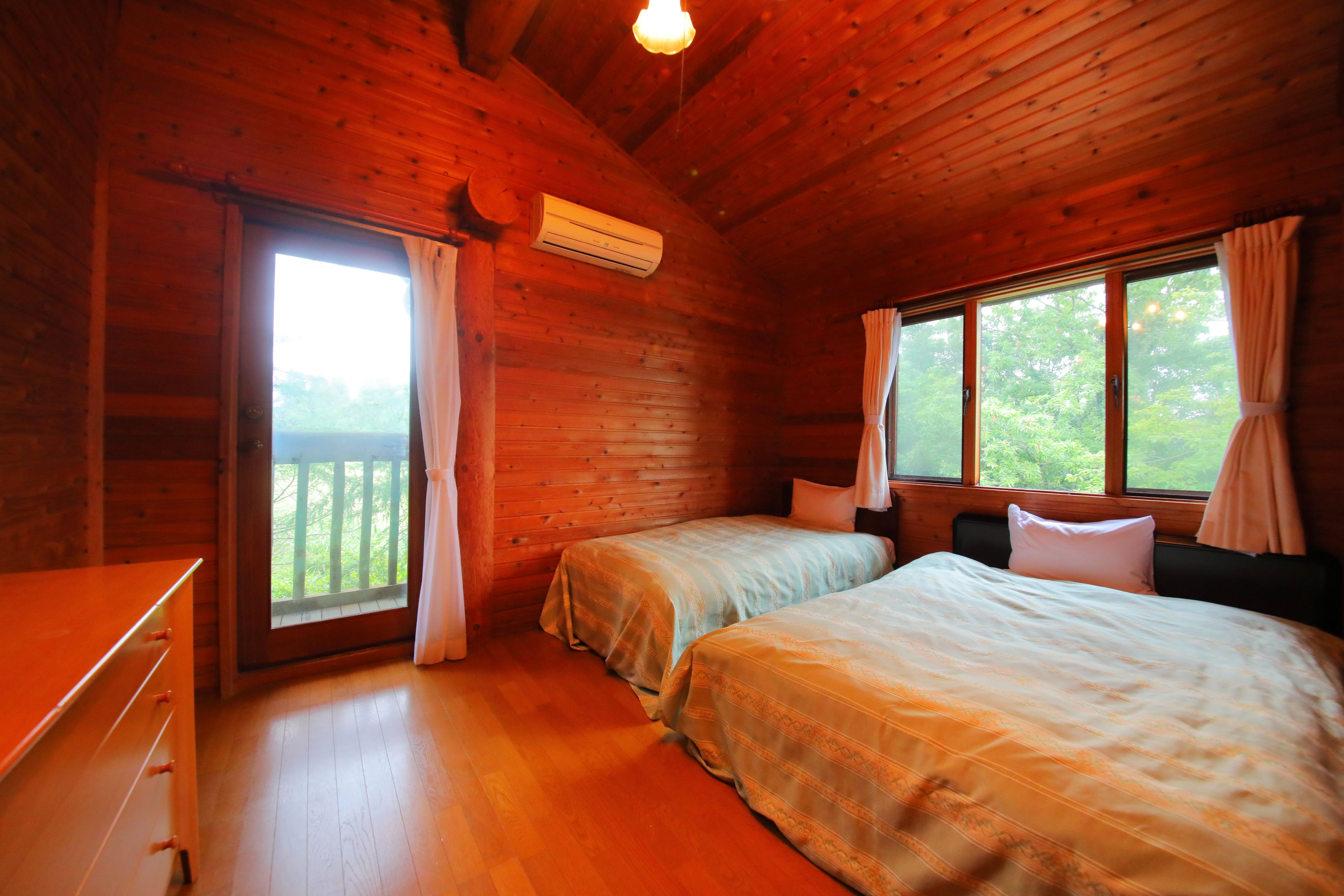 Een houten kamer met twee bedden, een dressoir en een raam met gordijnen.