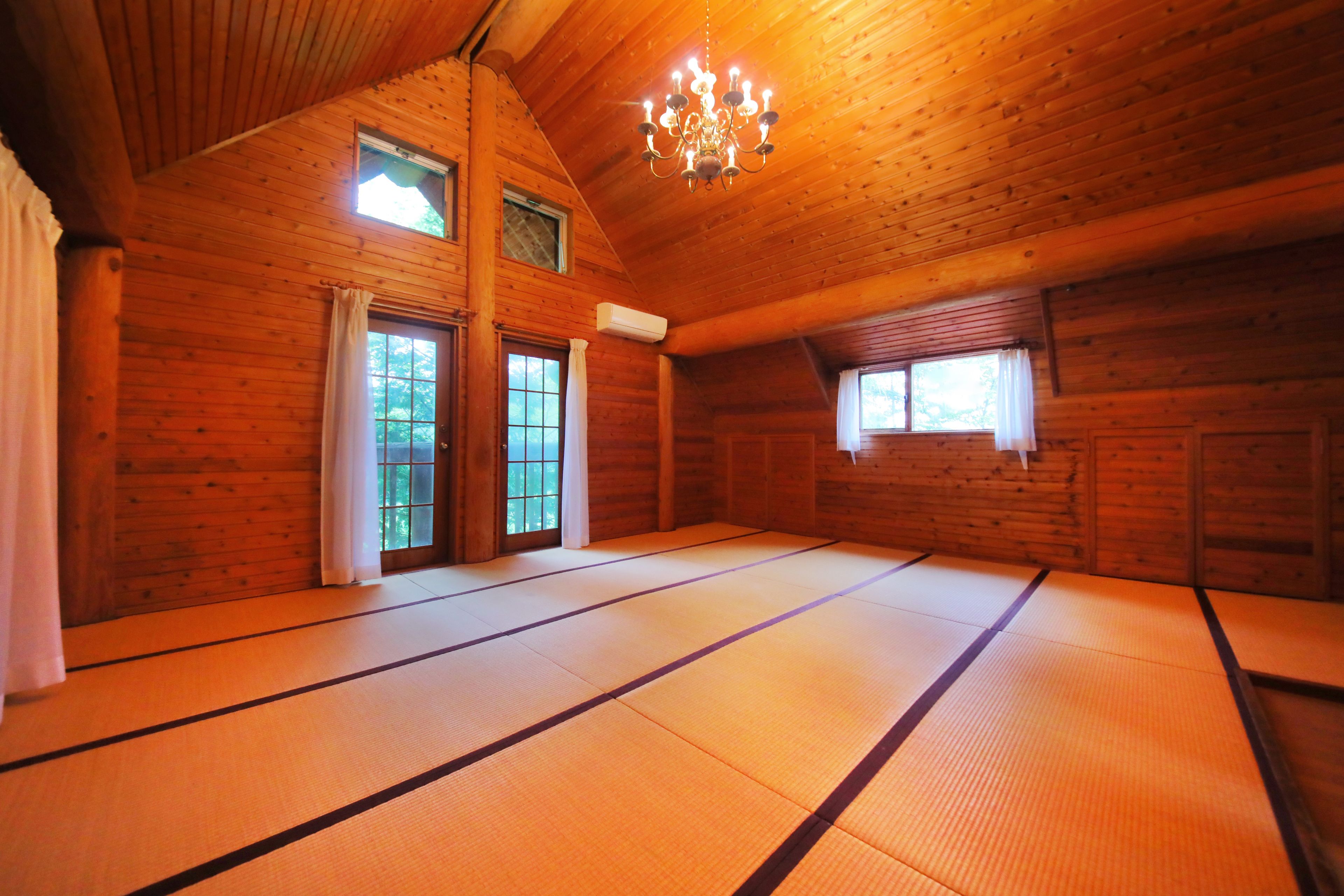 A room with tatami mats, wooden walls, a chandelier, and windows.
