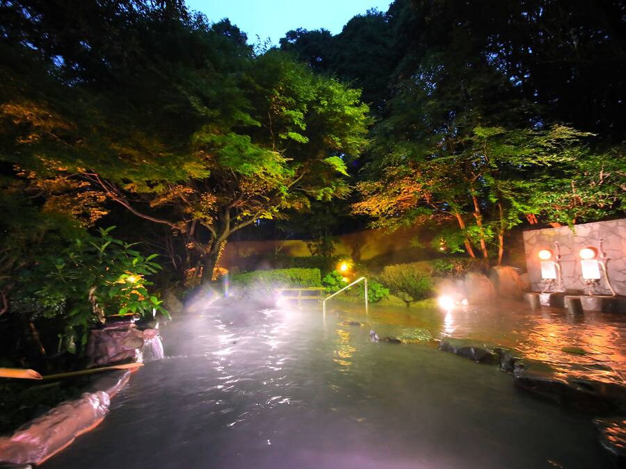 A hot spring area with a stone wall, wooden steps, and a small bridge.