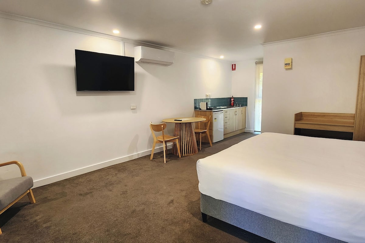 Habitació d'hotel amb llit, televisió penjada a la paret, petita cuina i zona de seients amb una cadira i taula.