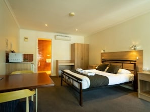 Habitación de hotel compacta con una cama individual, un escritorio pequeño y una kitchenette.