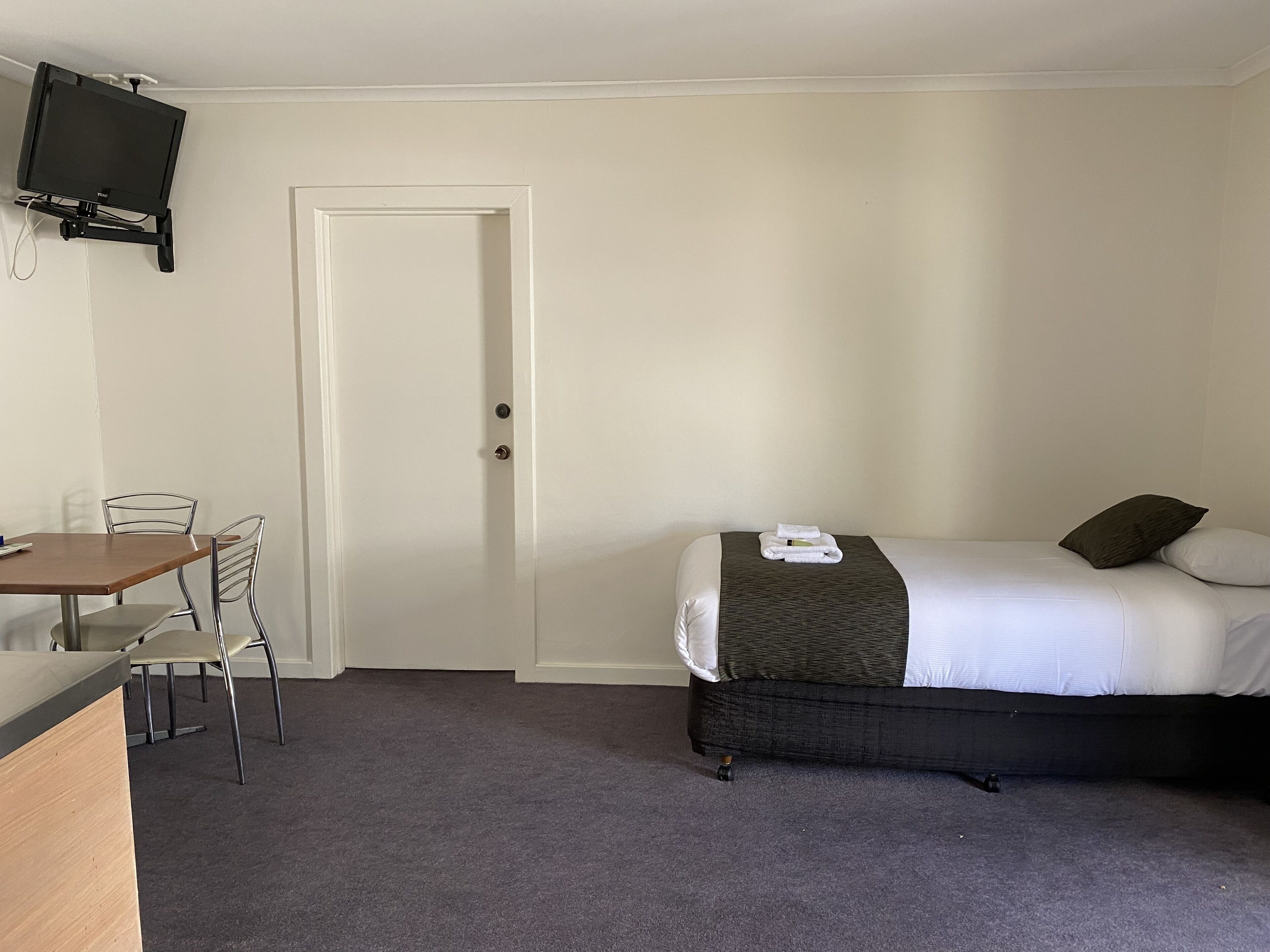 A hotel room with a bed, a desk, a chair, and a television mounted on the wall.