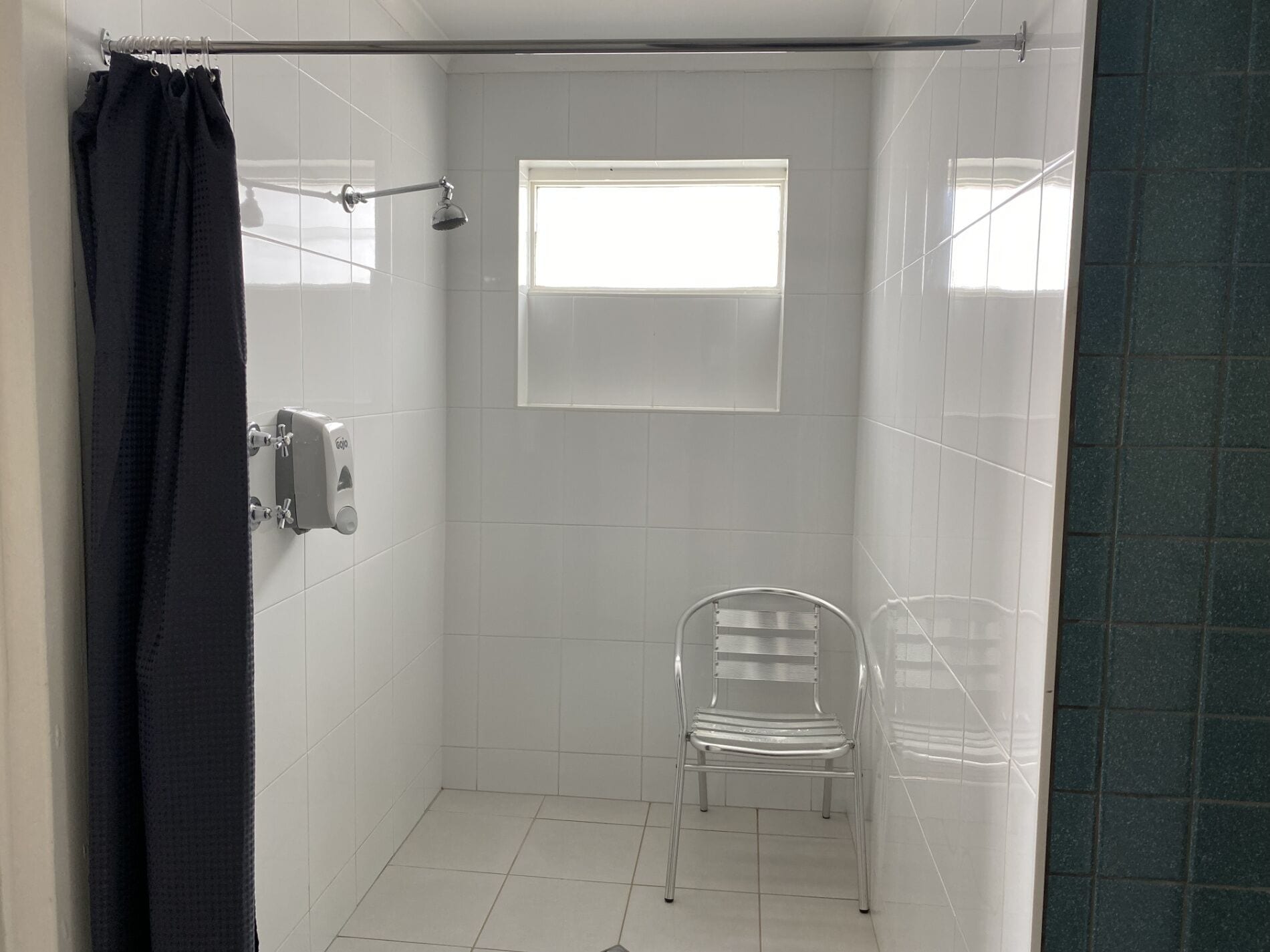 Un pequeño baño revestido con azulejos, con ventana, secamanos y una silla.