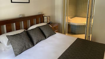 A hotel room with a bed, a nightstand, a framed picture, and a glass-enclosed shower area.