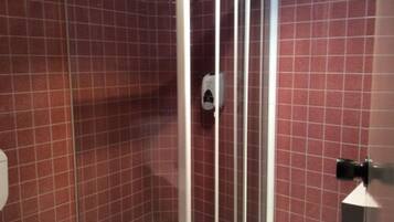 A bathroom with red tiled walls, a glass shower enclosure, and a white toilet.