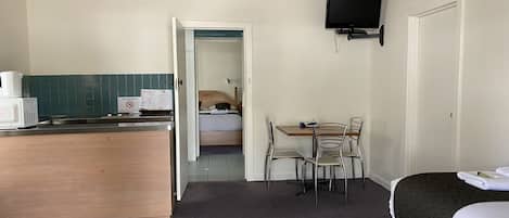 Una habitación de hotel con kitchenette, una cama, una mesa de comedor con sillas y un televisor montado en la pared.