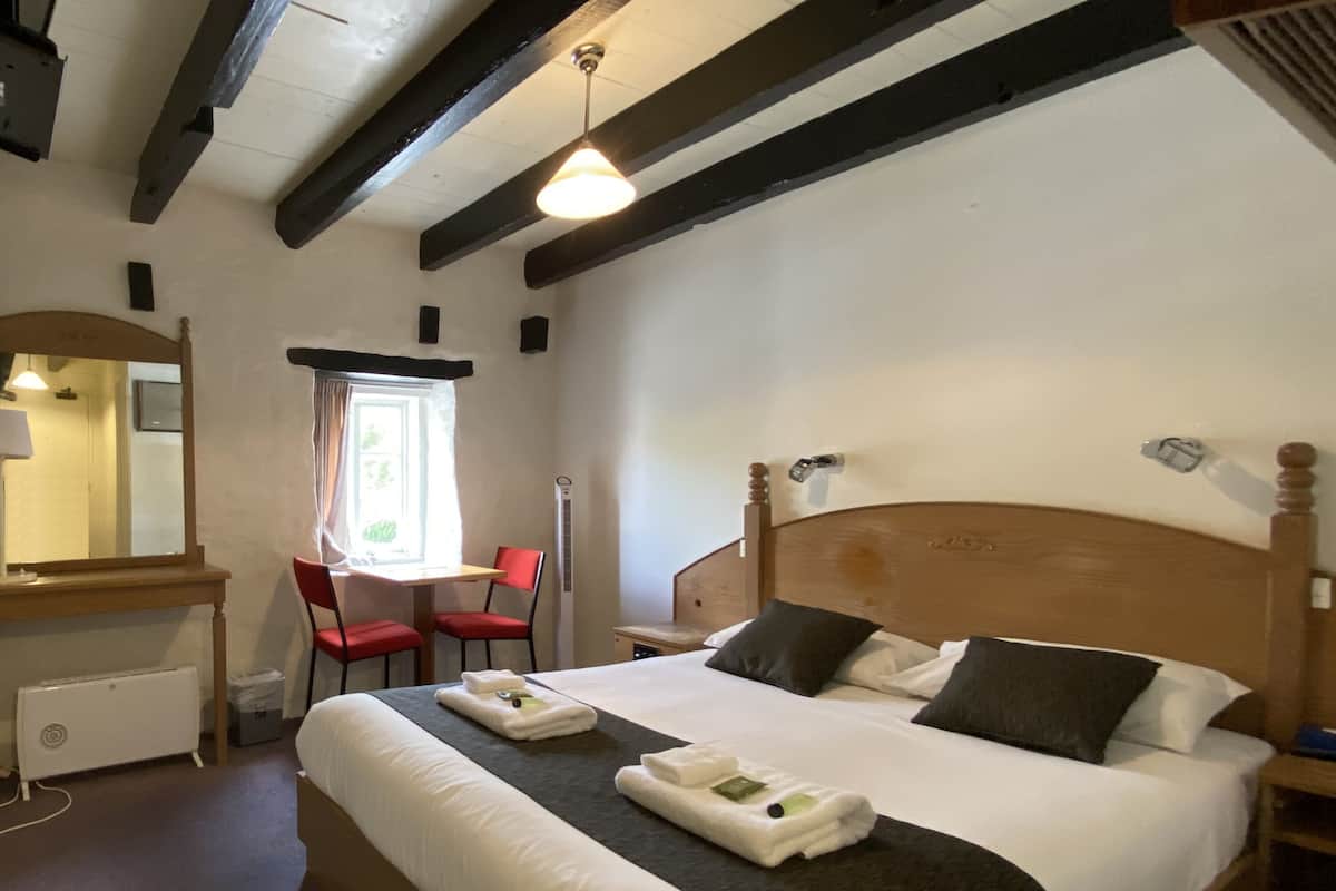 Habitació d'hotel amb un llit, una taula de treball, una cadira, una finestra i un ventilador de sostre.