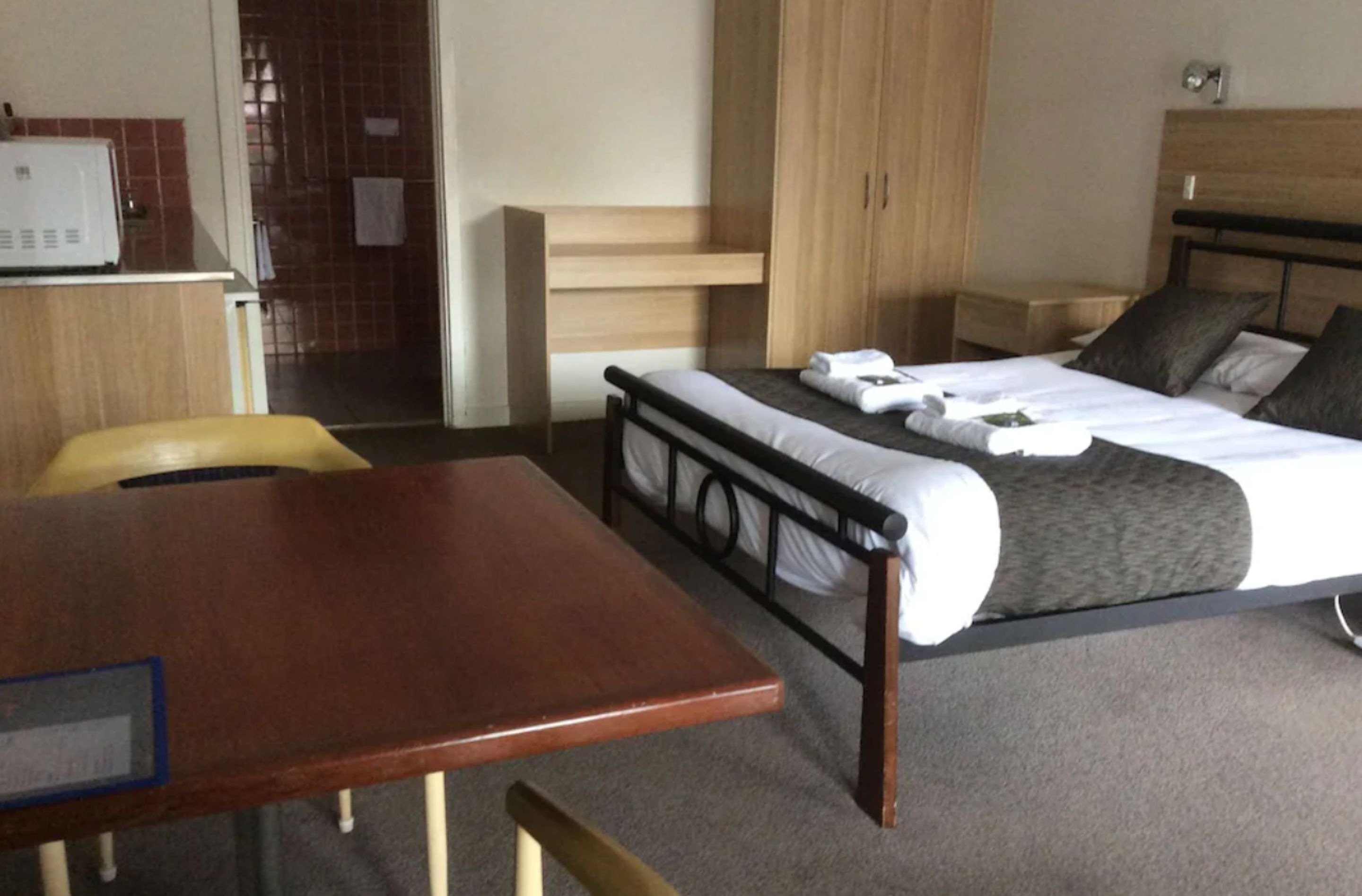 A hotel room with a bed, a wooden desk, a chair, and a wardrobe.