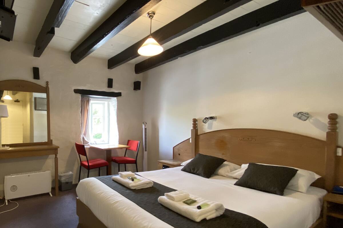 Habitació d'hotel amb un llit gran, una taula de treball amb una cadira, una finestra amb cortines i un ventilador de sostre.