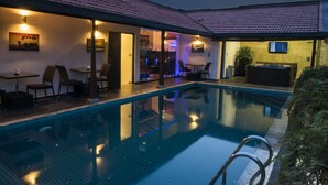 A swimming pool with a tiled deck, outdoor seating, and ambient lighting. - D Villas (Sri Jayawardenepura Kotte)