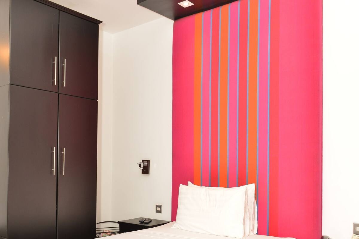 A modern bedroom with a bed, a wardrobe, a nightstand, and a wall with vertical stripes.
