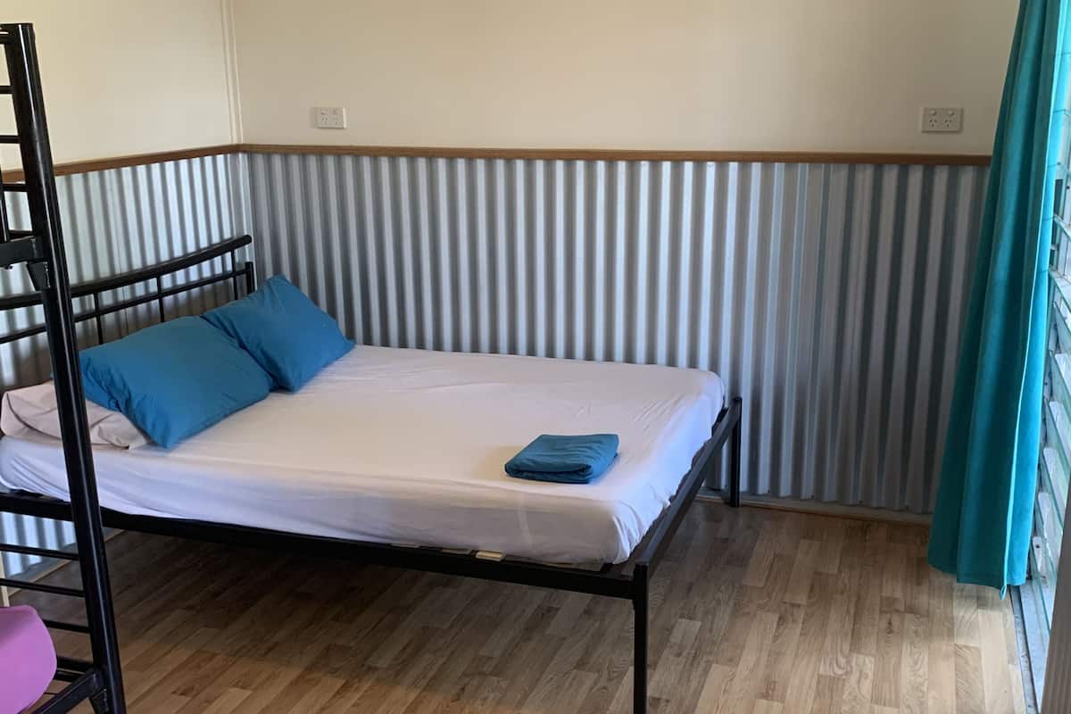 A single bed with a metal frame, a wooden floor, a bunk bed with a pink chair, and a striped curtain.