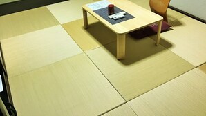 Quarto com piso de tatame, uma pequena mesa de madeira com um controle remoto e uma cadeira.