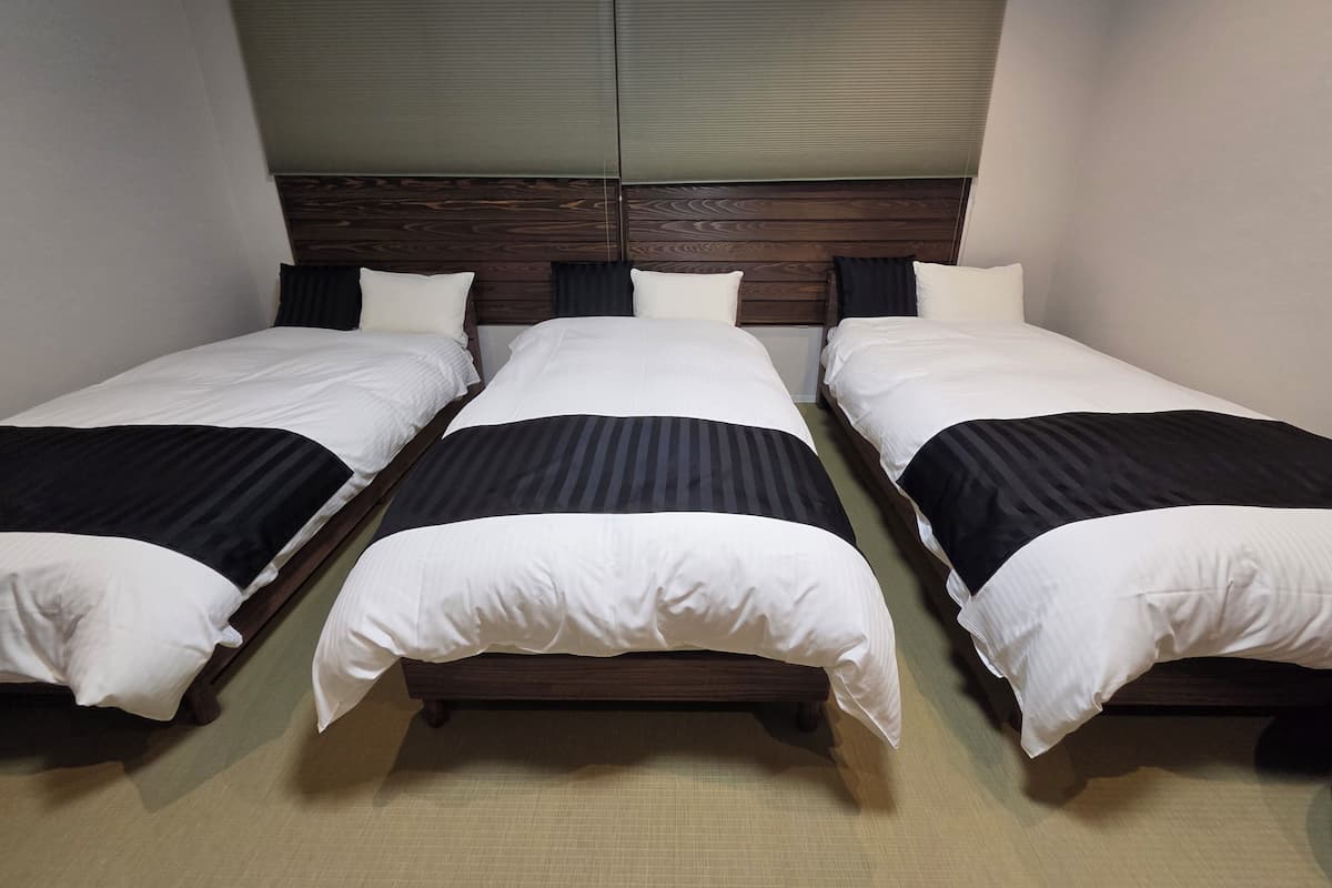 A hotel room with three single beds, wooden headboards, and a large window with blinds.