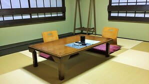Um espaço com tatames, mesa de madeira, cadeiras, escada e janela com padrão de grade.
