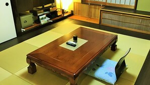 Um quarto tradicional com tatames, uma mesa de madeira, um controle remoto e um pequeno objeto preto sobre a mesa.