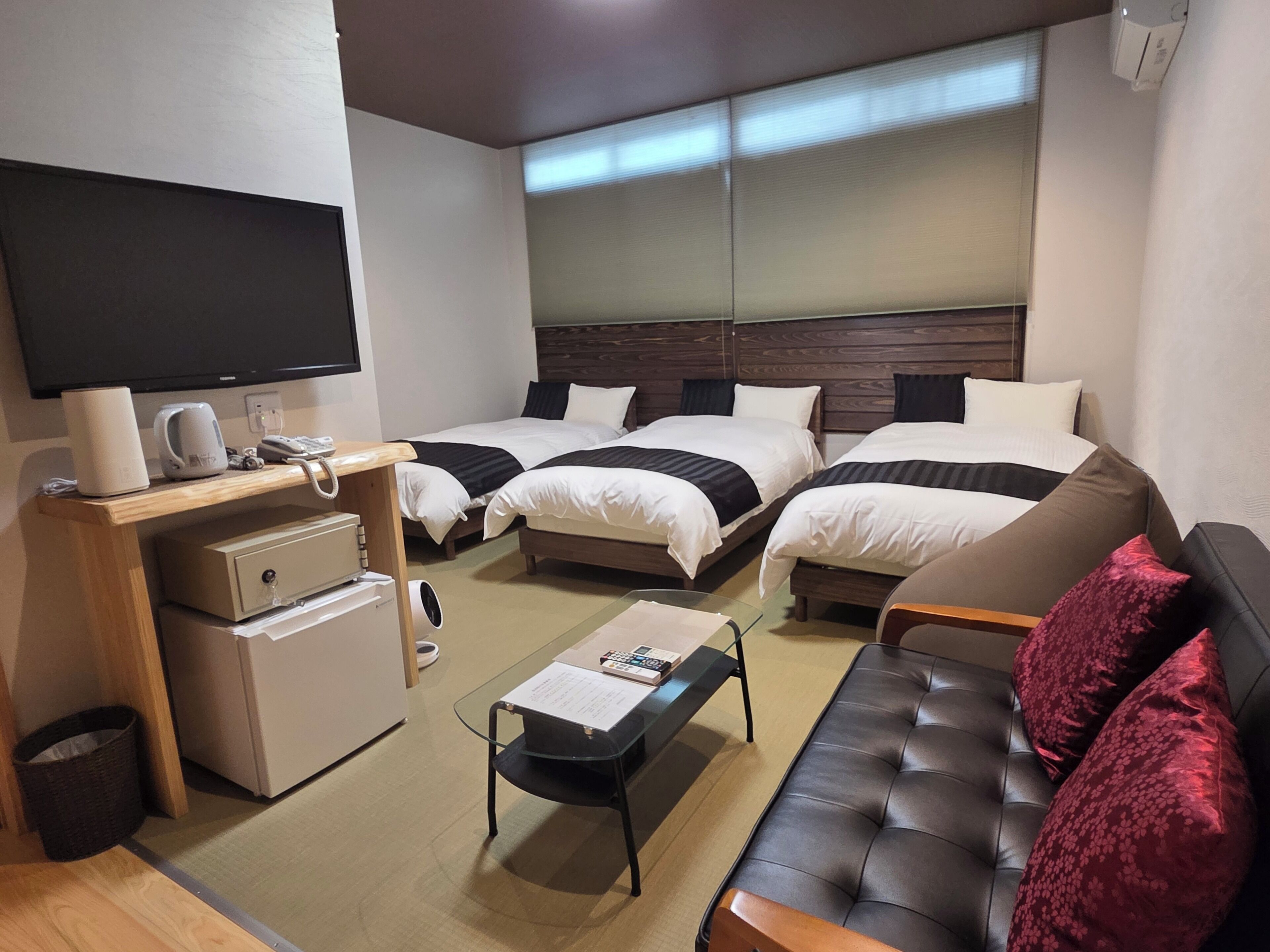A hotel room with two beds, a sofa, a small table, a TV, a desk with a computer, and a trash bin.
