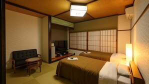 Quarto tradicional japonês com tatames, uma mesa baixa com almofada, um sofá e duas camas com futons.