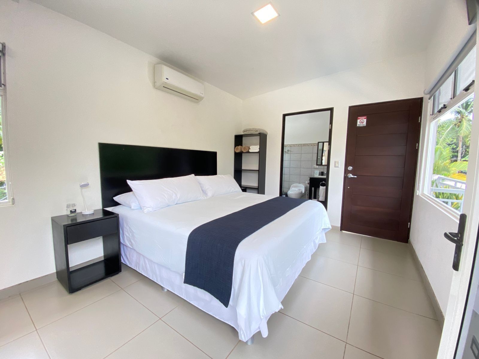 Een hotelkamer met een bed, nachtkastje en een raam met uitzicht op groen.