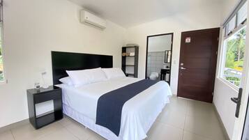 Een hotelkamer met een bed, nachtkastje en een raam met uitzicht op groen.