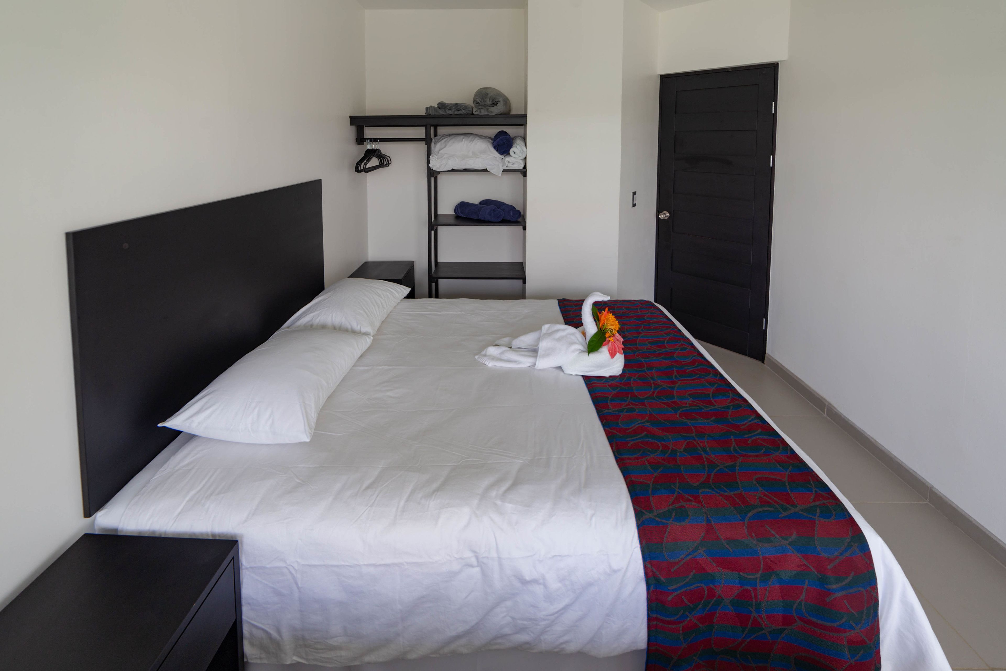 Un lit bien fait, avec du linge de lit blanc, une couverture à motifs rouges et bleus, et un arrangement floral décoratif.