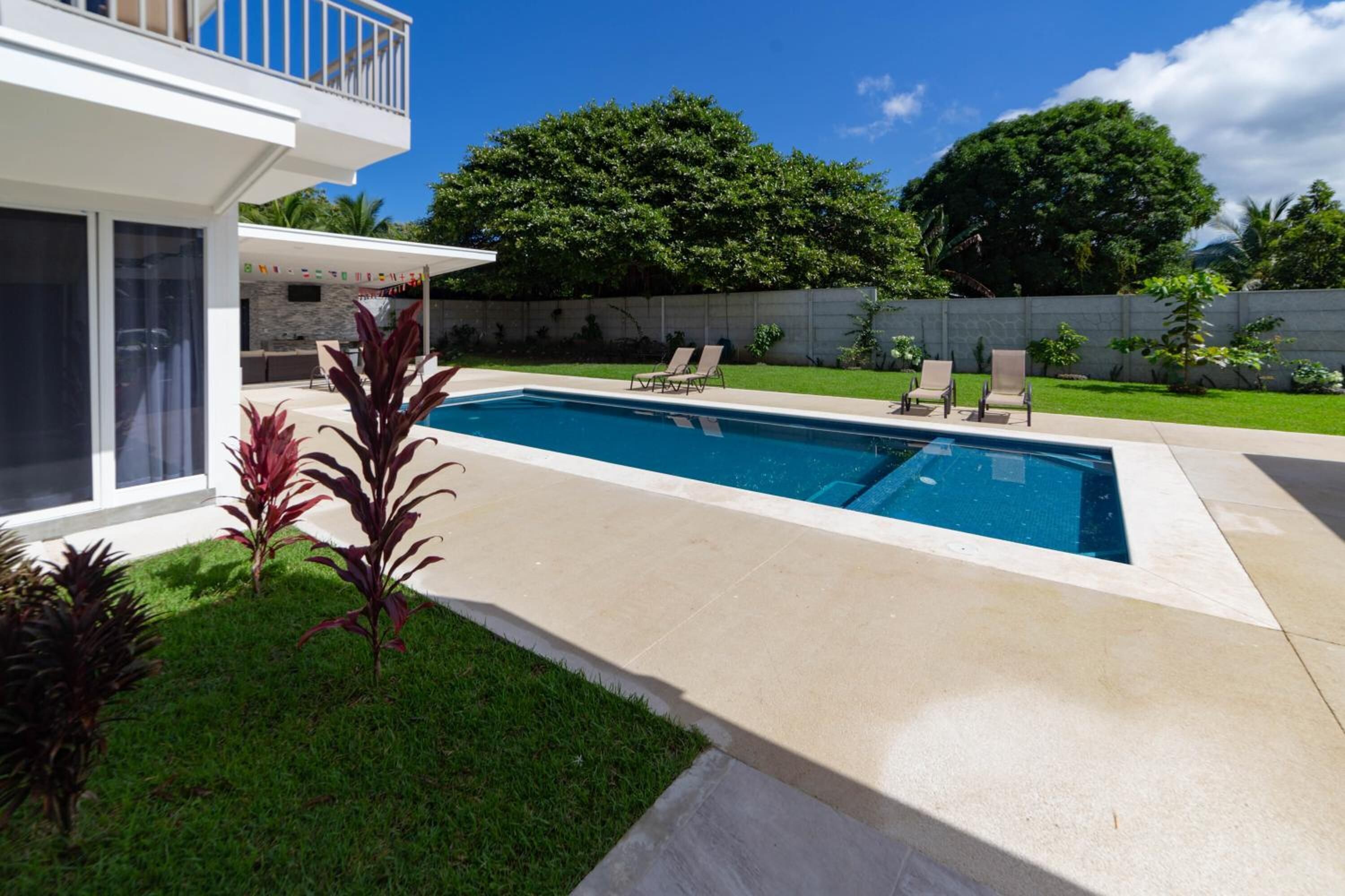 Ein modernes Haus mit Swimmingpool, überdachter Terrasse und gepflegtem Rasen.