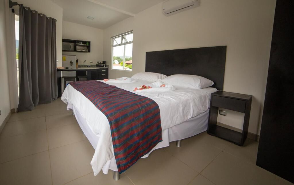 A bedroom with a bed, a bedside table, a desk with a chair, and a window.