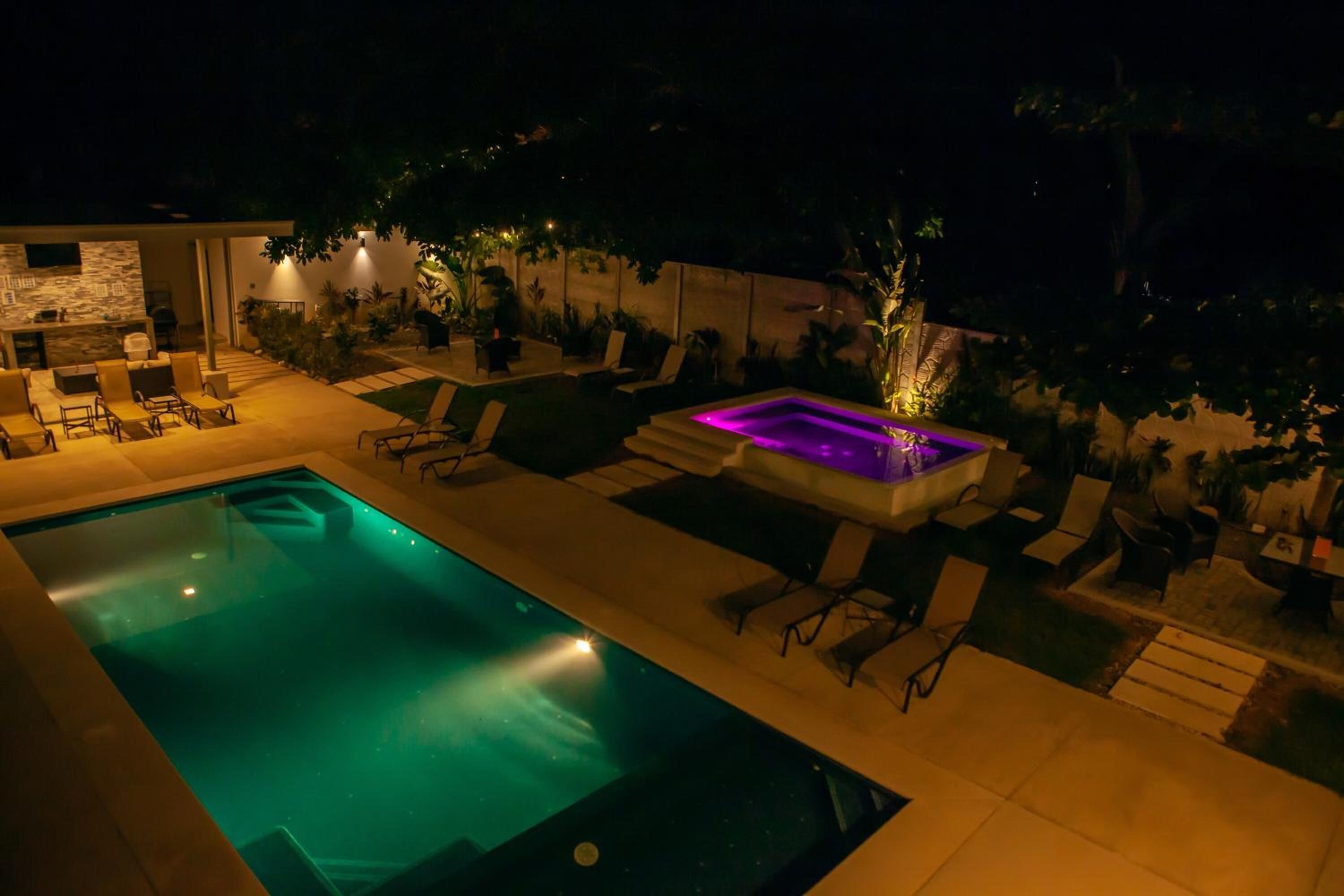A swimming pool with lounge chairs and a hot tub area, surrounded by potted plants and a stone wall.