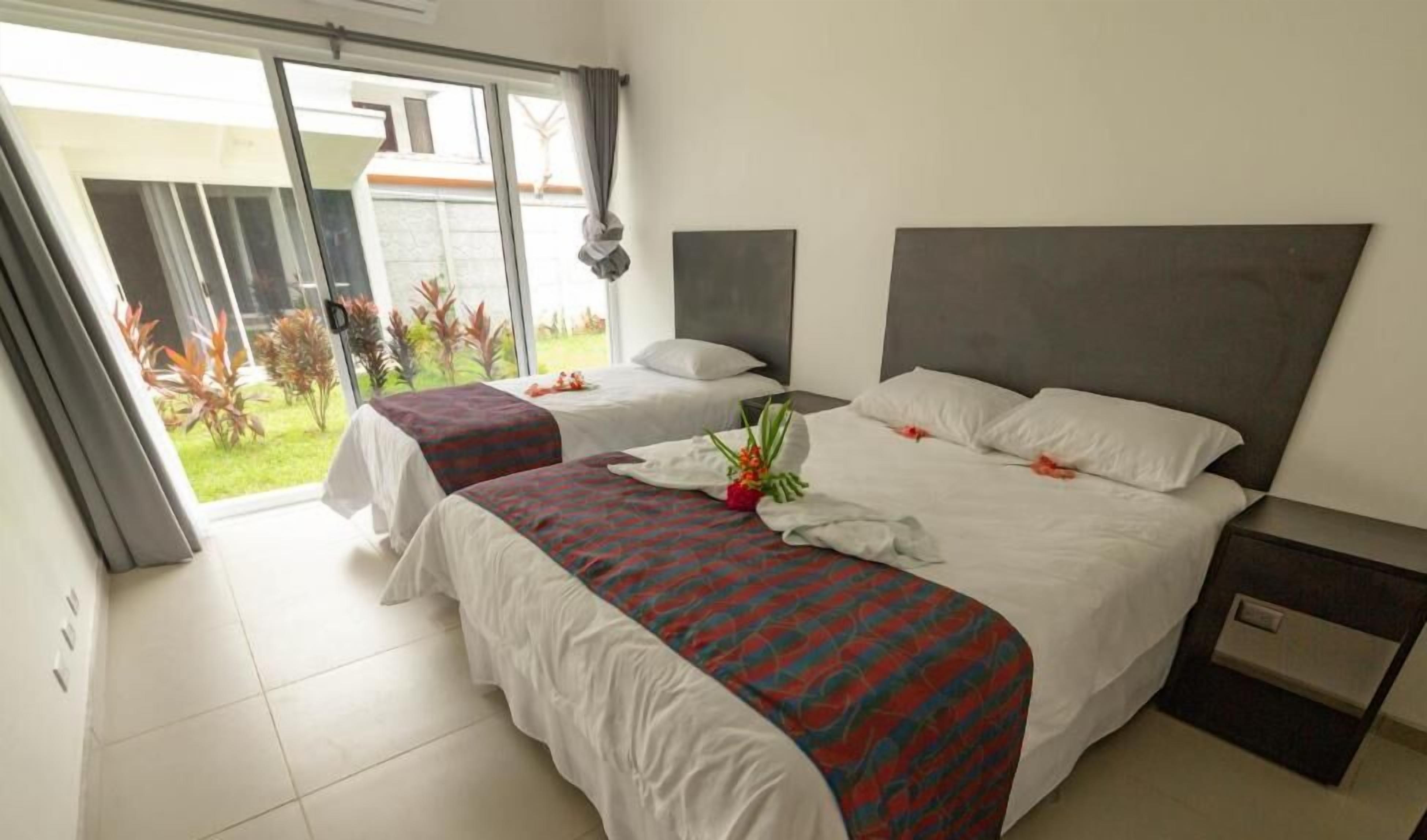 Een hotelkamer met twee bedden, een groot raam en uitzicht op een tuin.