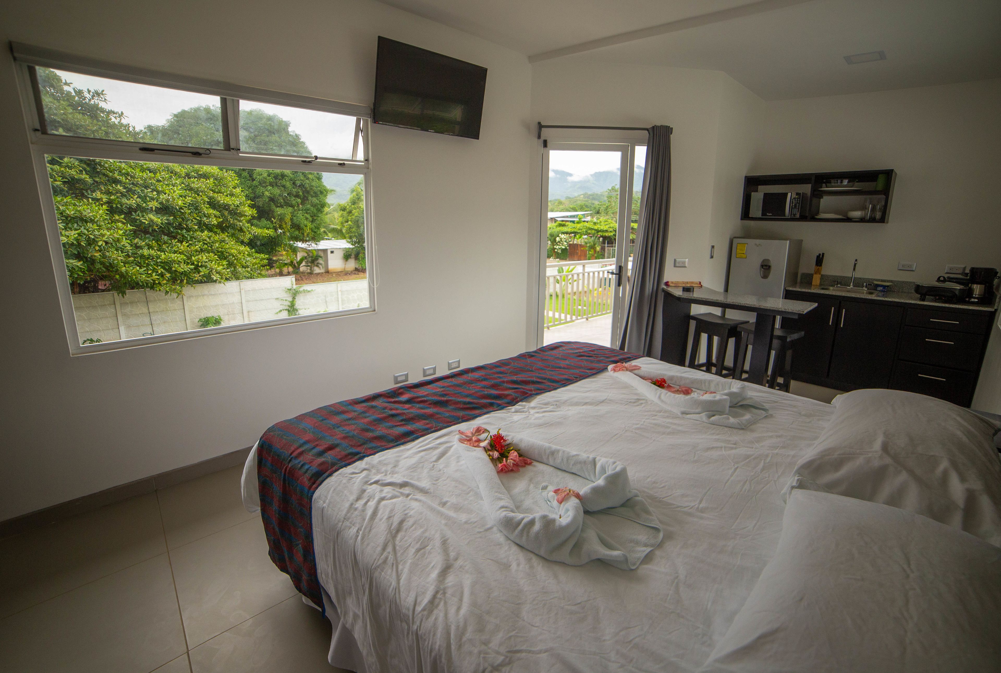 A hotel room with a bed, a desk, a microwave, and a balcony with a view of greenery.