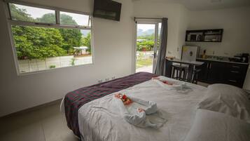 A hotel room with a bed, a desk, a microwave, and a balcony with a view of greenery.