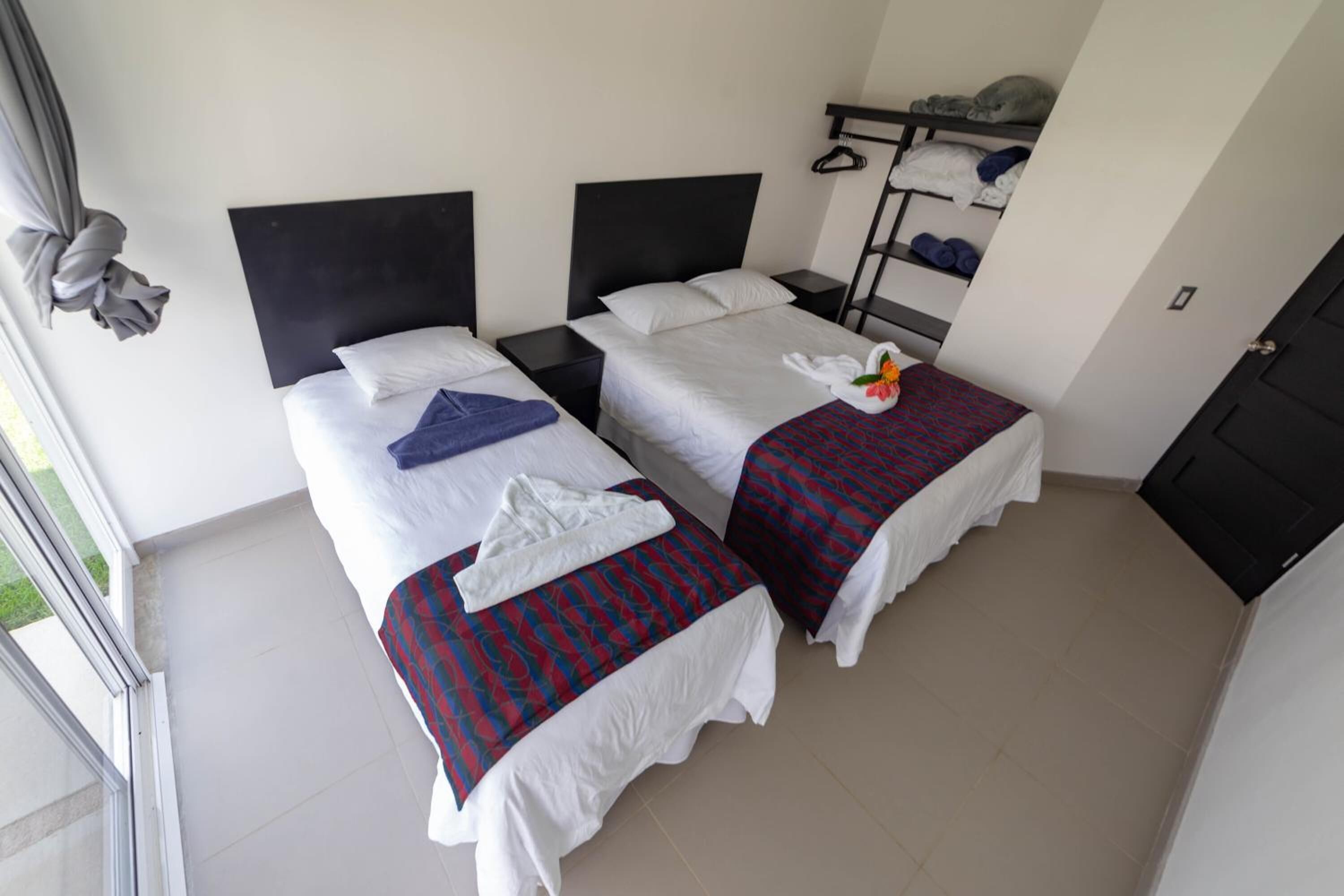 Une chambre d’hôtel avec deux lits simples, une armoire et une fenêtre avec des rideaux.