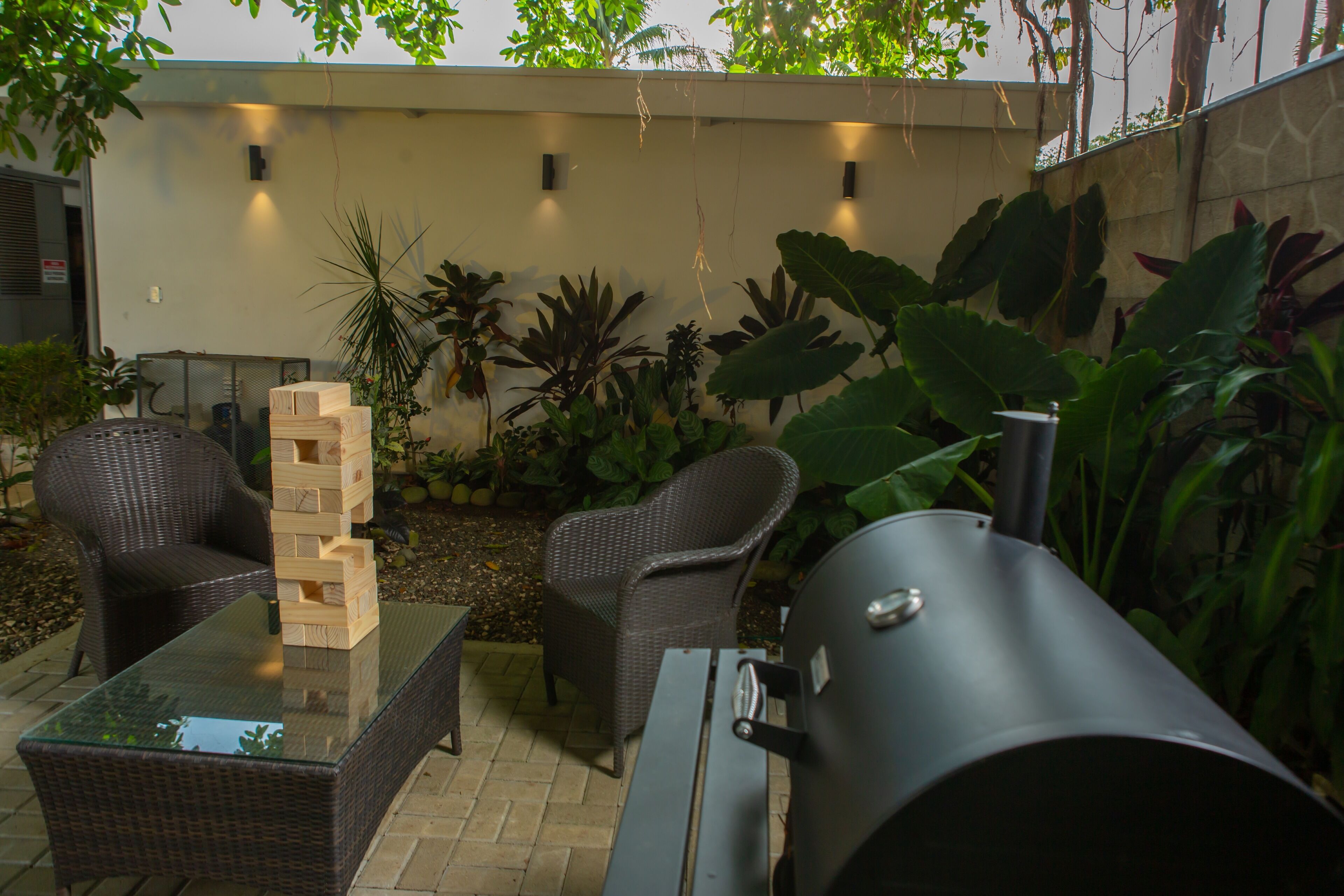 An outdoor patio with wicker furniture, a glass-top table, and a grill.