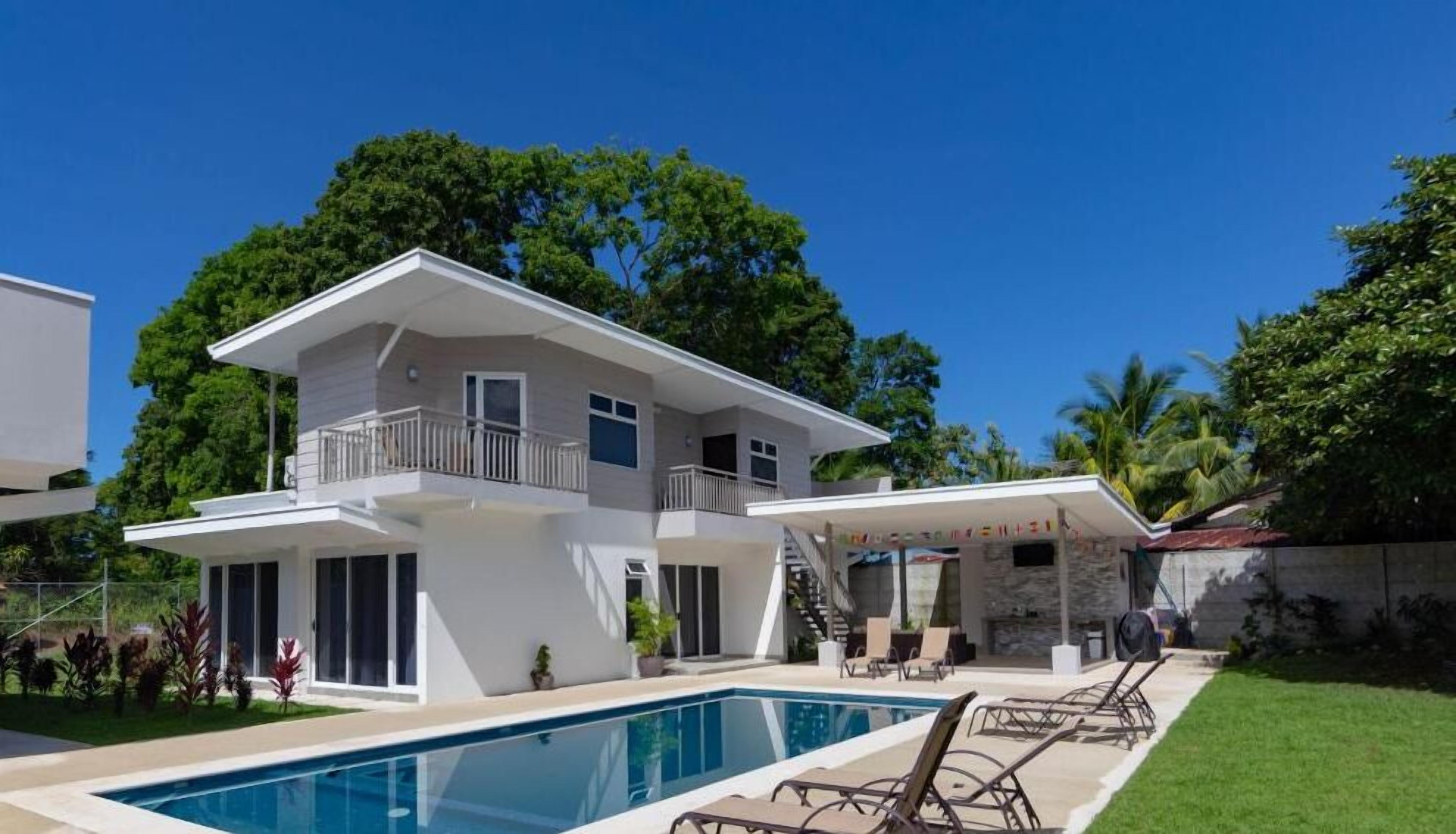 Una casa de dues plantes amb piscina, un porxo cobert i una escala que condueix a un balcó.
