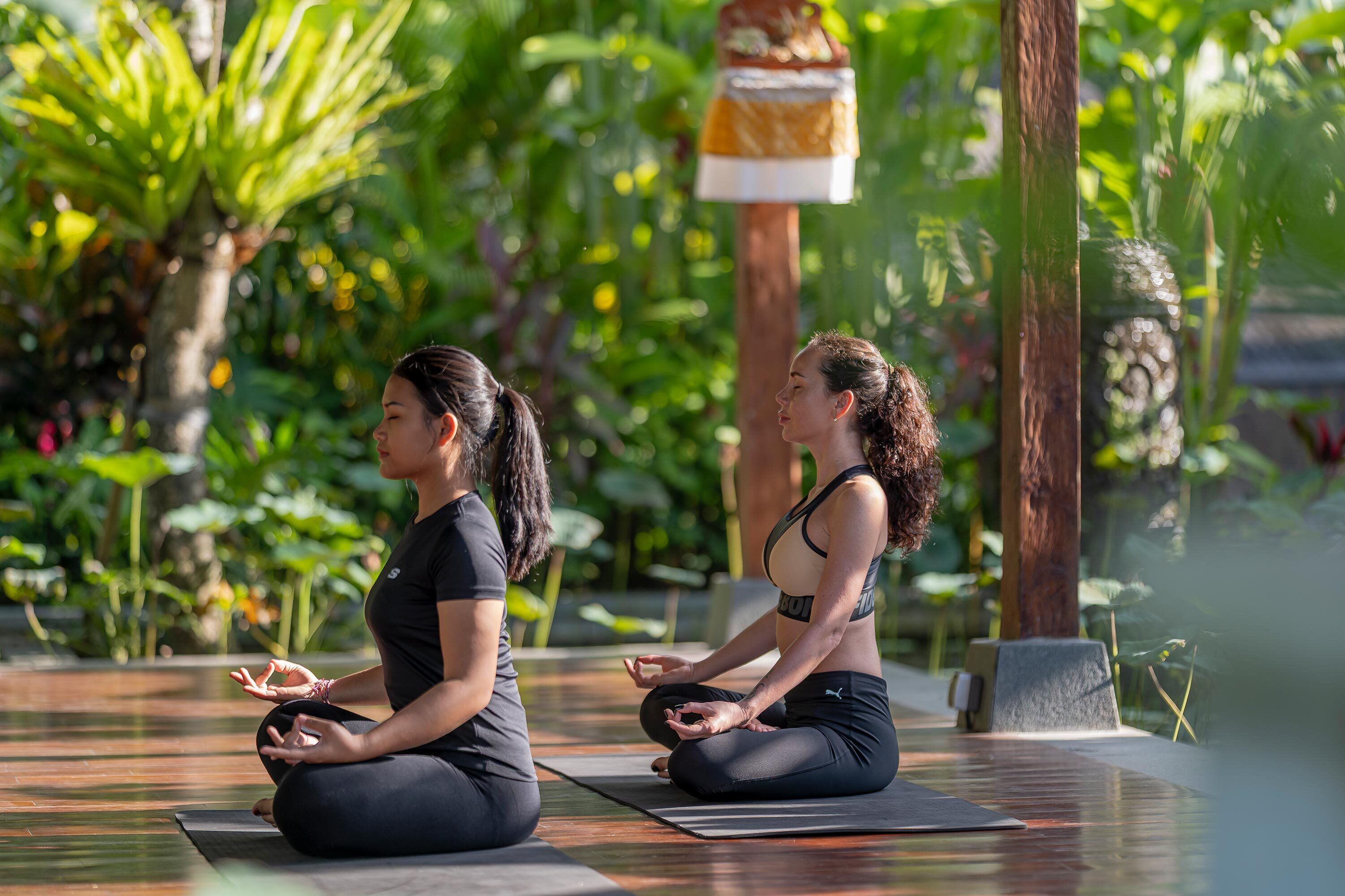 Twee personen zitten op yogamatten in een groene buitenomgeving.