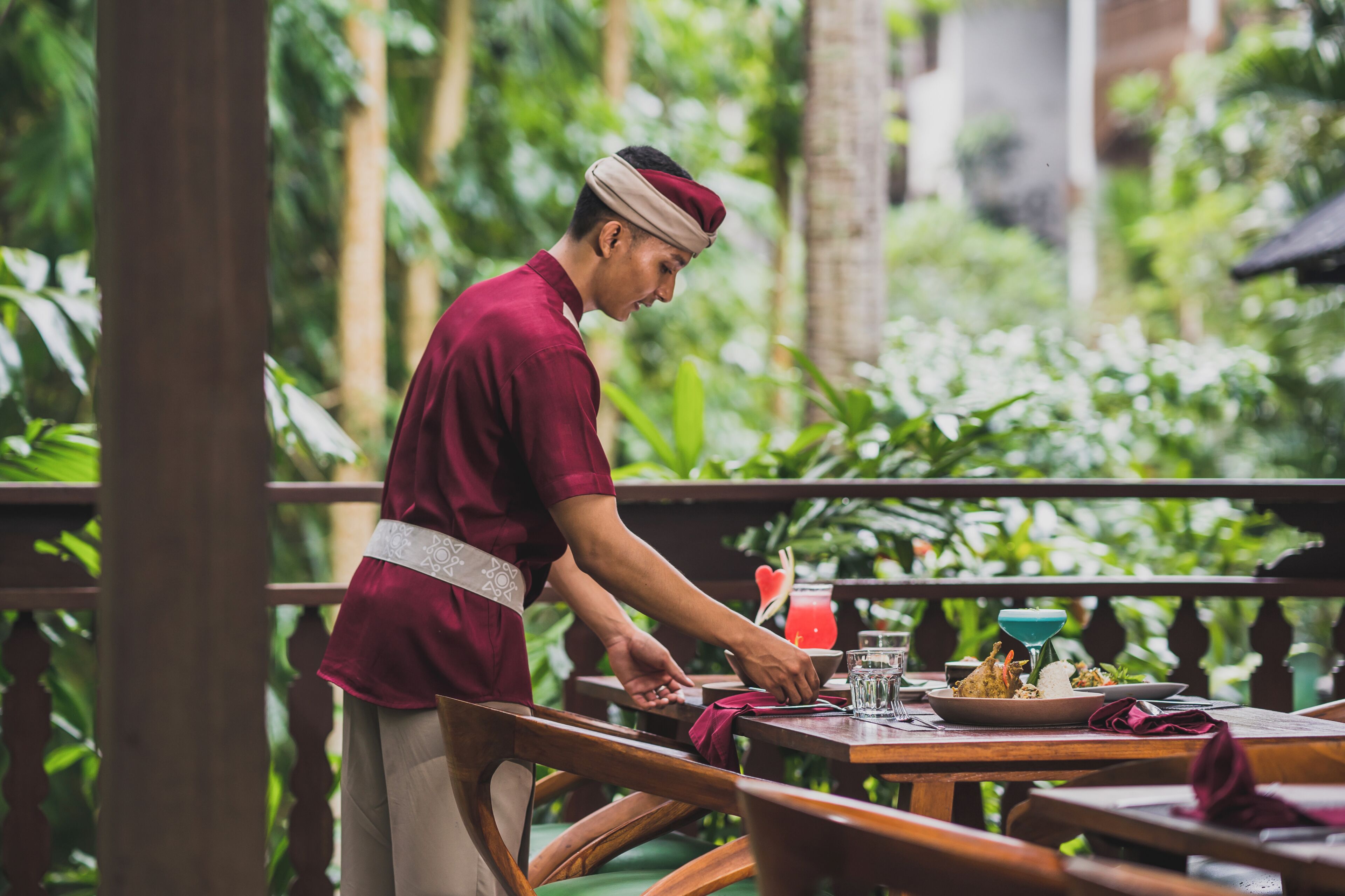 Una persona sirviendo comida en una mesa al aire libre, con un paisaje tropical de fondo.