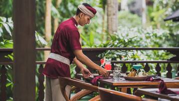 Una persona sirviendo comida en una mesa al aire libre, con un paisaje tropical de fondo.