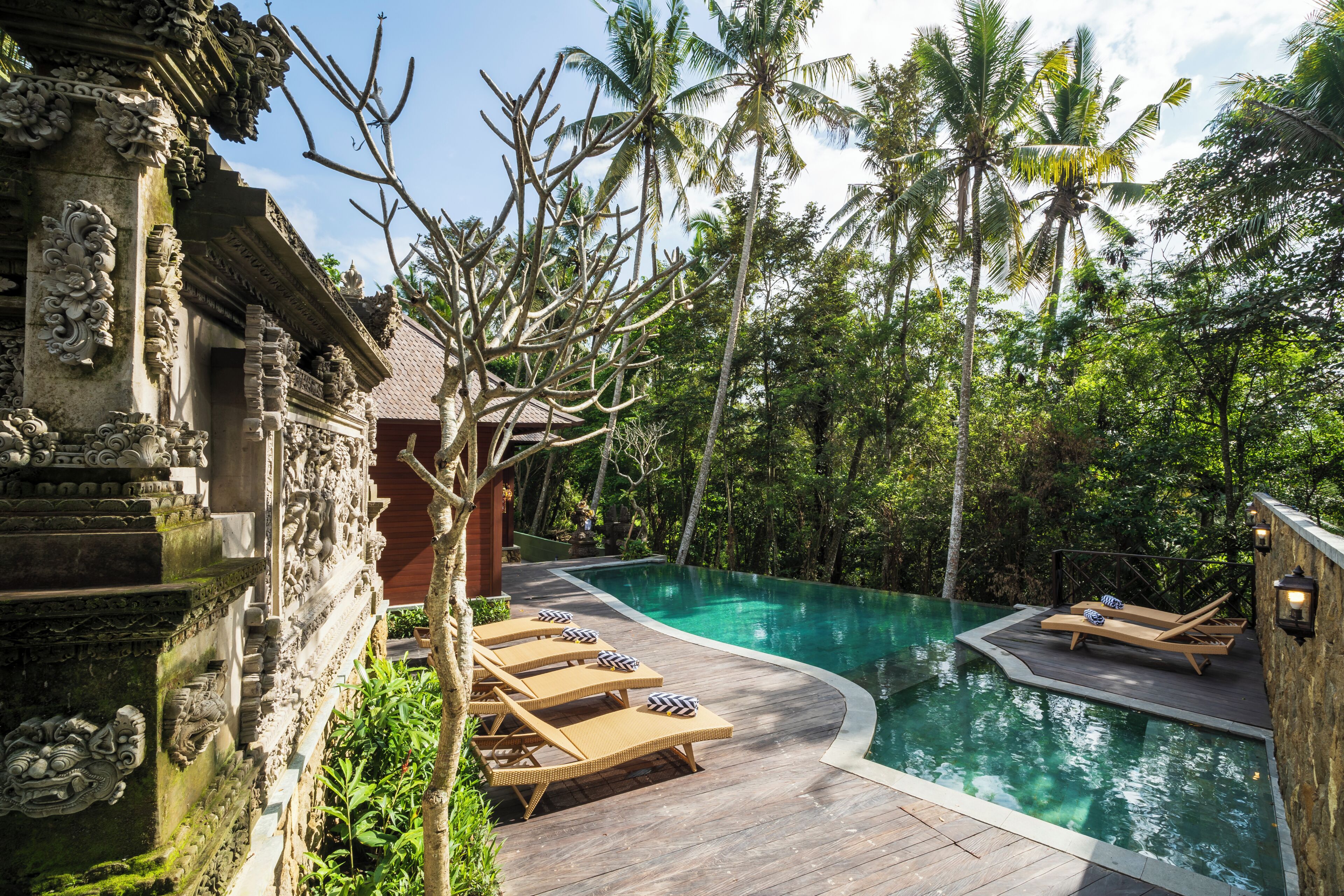 A pool area with lounge chairs and a stone building with intricate carvings.