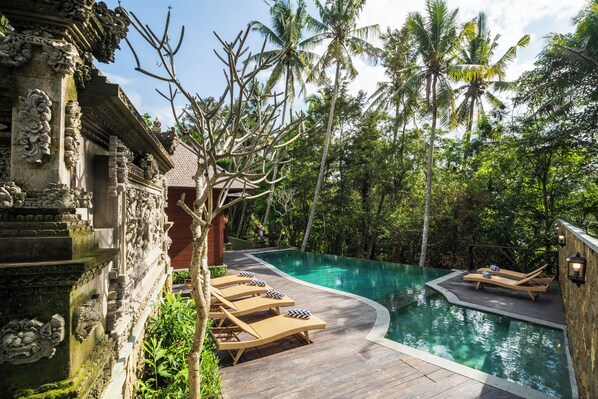 A pool area with lounge chairs and a stone building with intricate carvings. - Arkamara Dijiwa Ubud (Ubud)