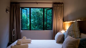 A bedroom with a large window, a bed with pillows, and a bedside table with a lamp. - Africa's Eden Guesthouse (Pietermaritzburg)