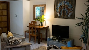 A living room with a TV, a dining table with chairs, a sofa, and a cabinet. - Africa's Eden Guesthouse (Pietermaritzburg)