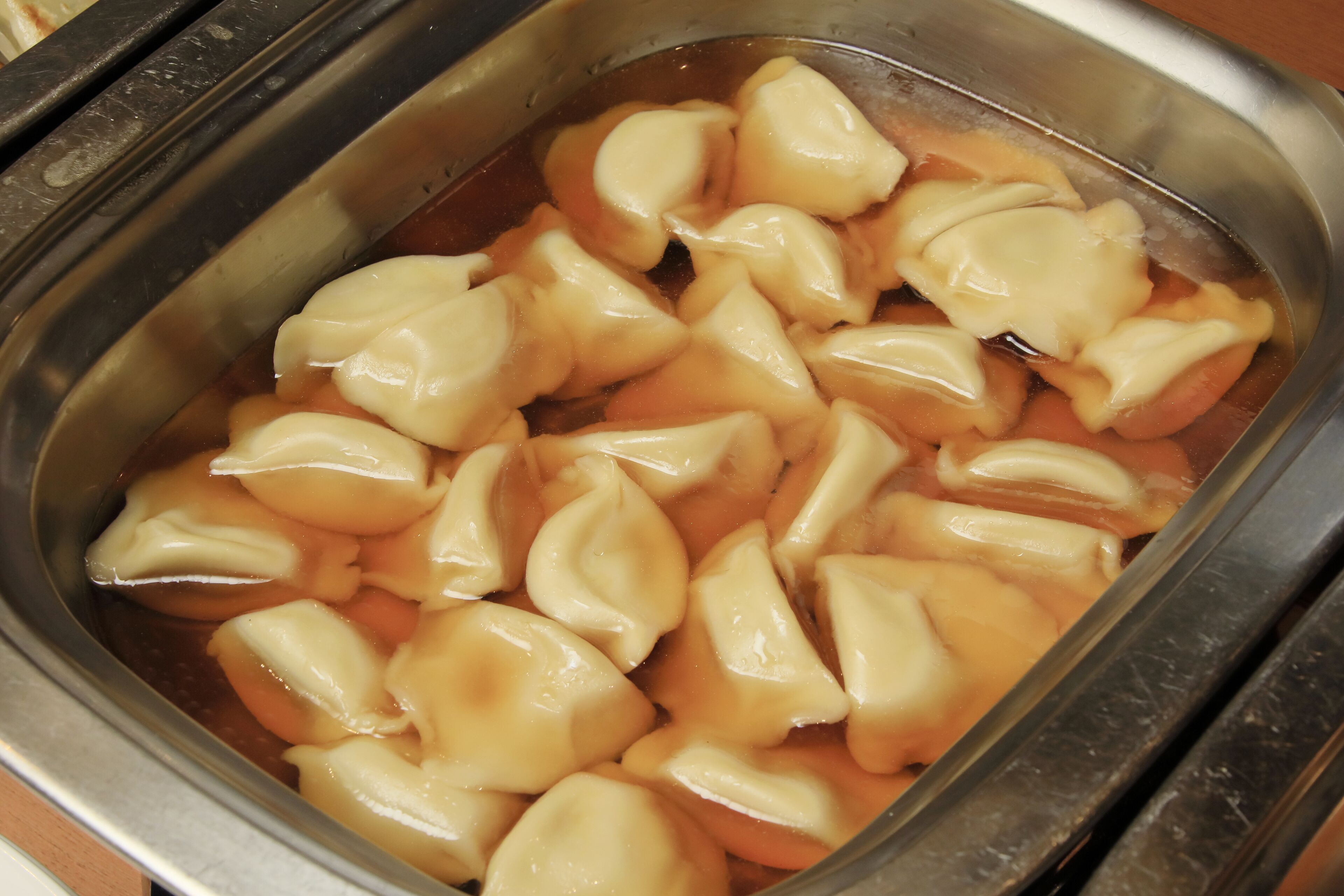 Een metalen bak gevuld met dumplings in een vloeistof.