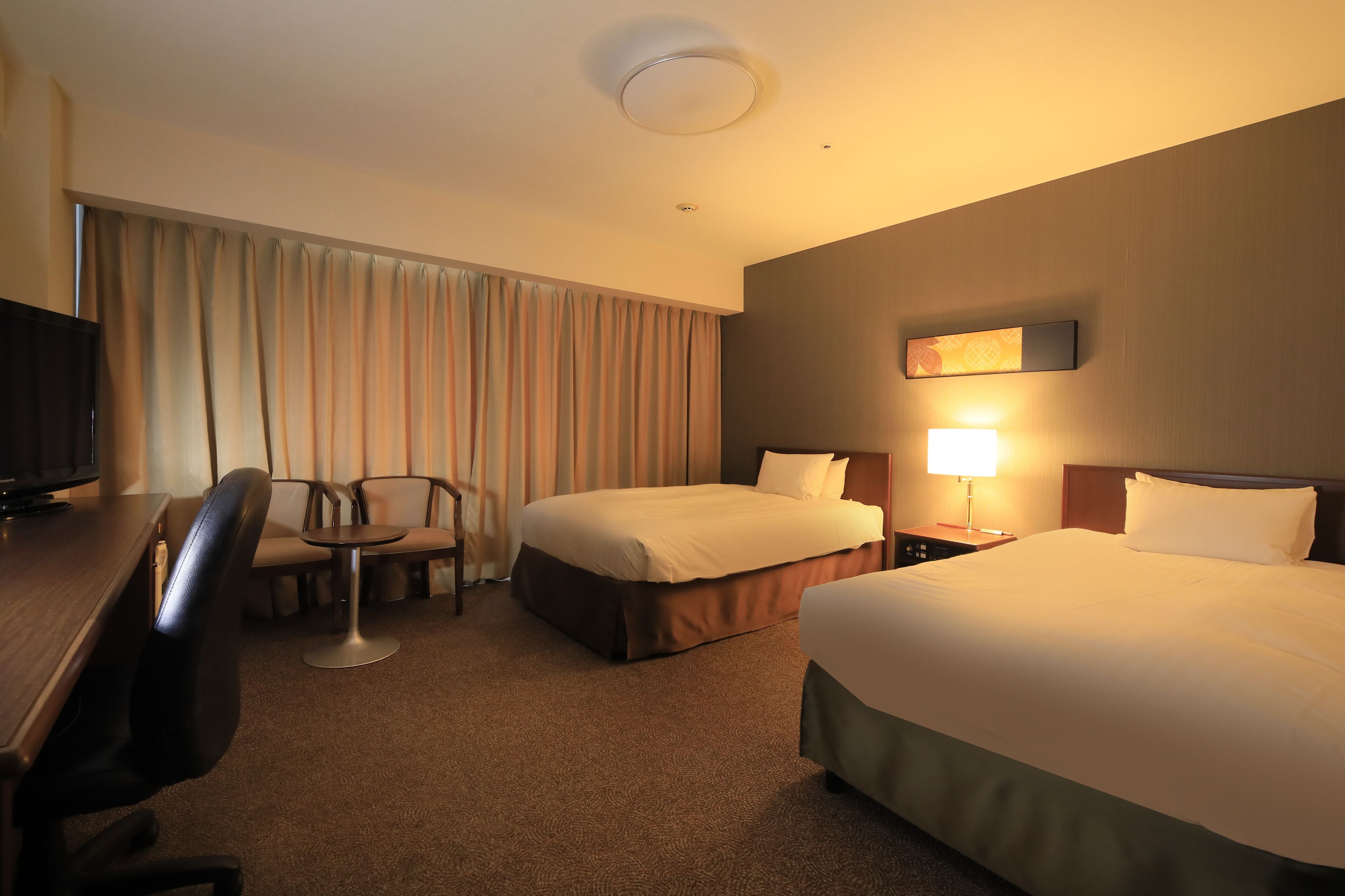 Ein Hotelzimmer mit zwei Betten, einem Schreibtisch, einem Sessel, einem Fernseher und einer Lampe.