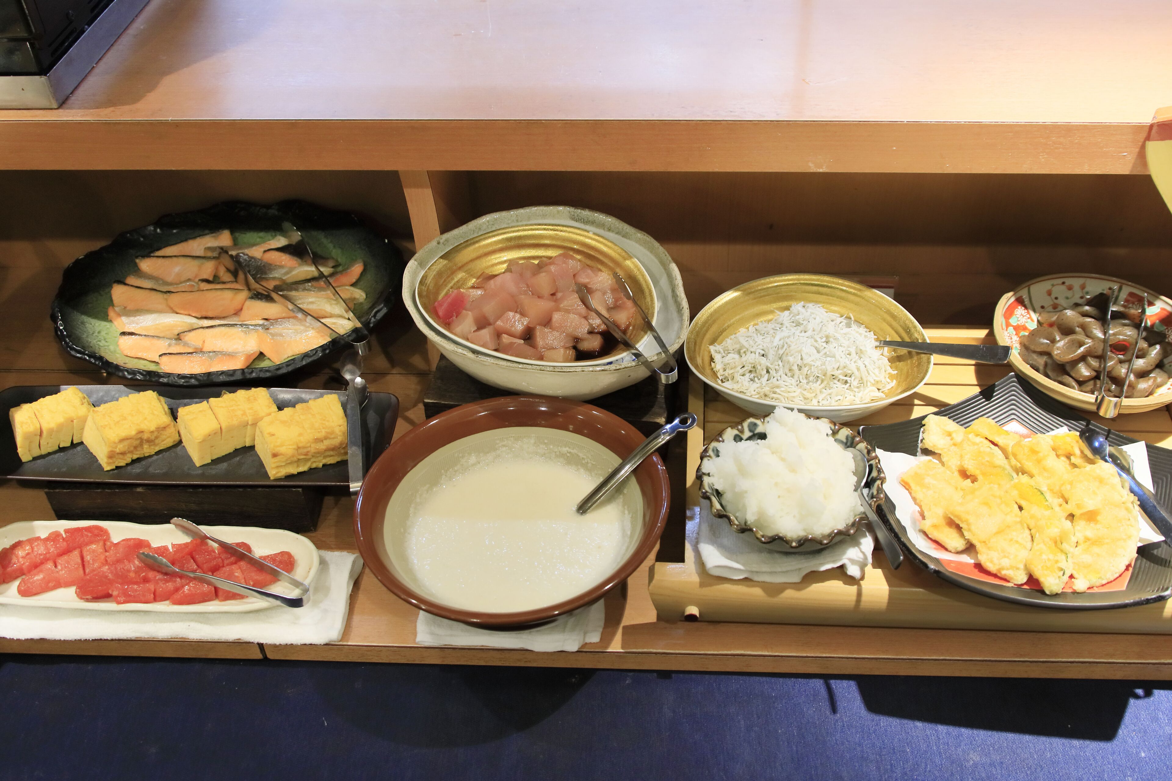 Un buffet proposant divers plats, notamment du poisson tranché, du riz et d’autres aliments préparés.