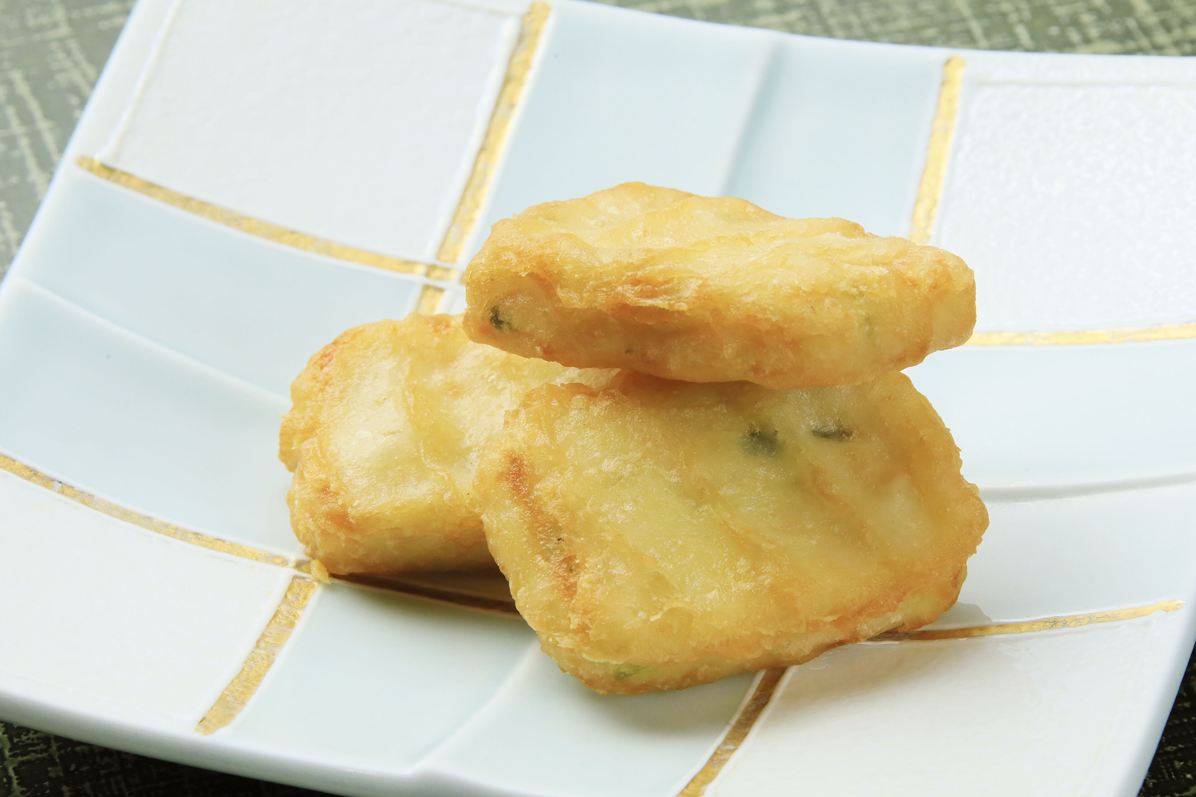 A white plate with a gold rim, holding three golden-brown fried items.
