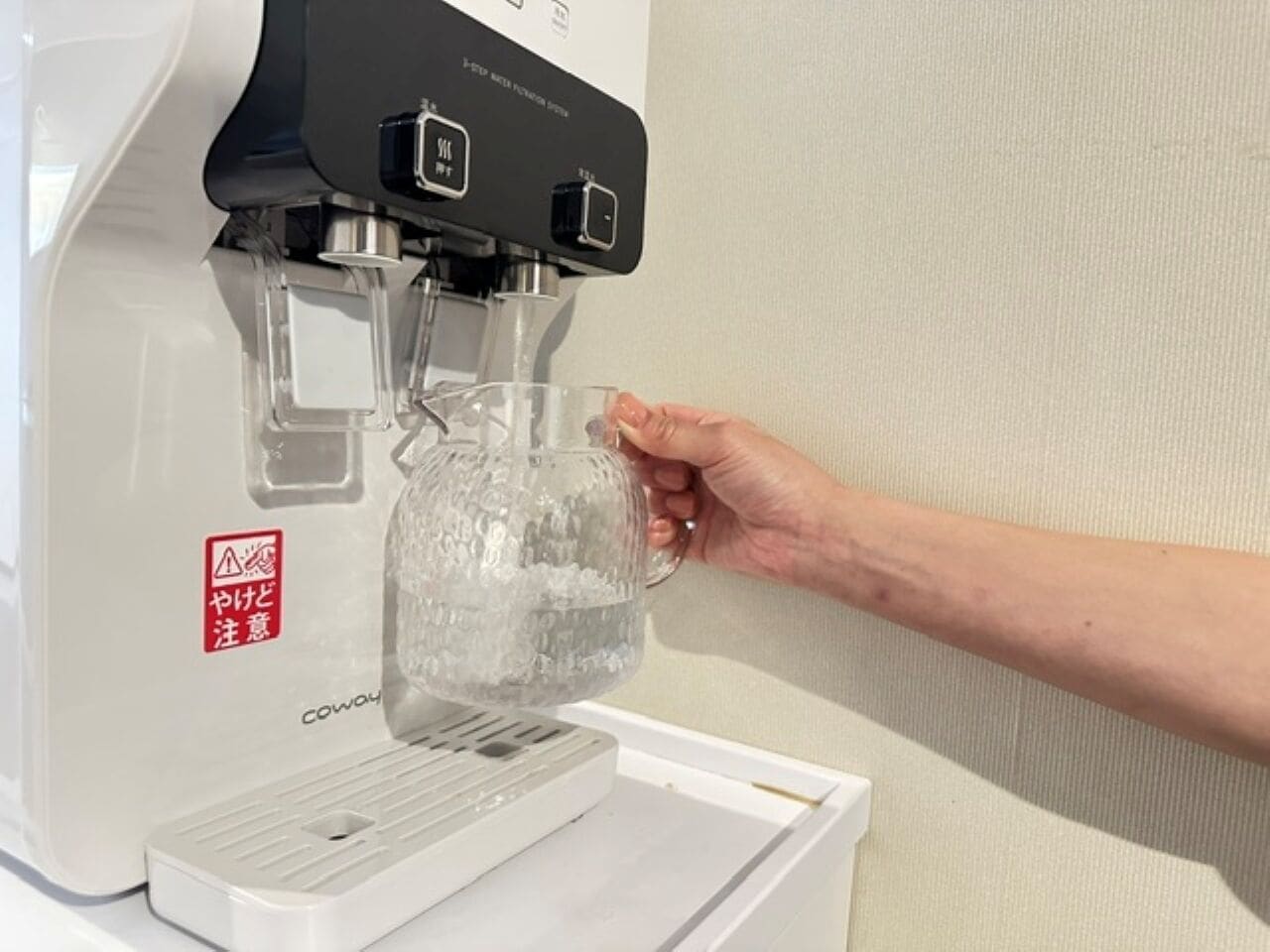 Une main tenant une tasse en verre sous un distributeur d’eau.